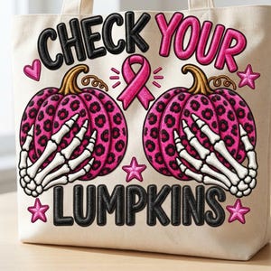 以下が含まれることがあります： 黒い文字で「CHECK YOUR LUMPKINS」と刺繍されたクリーム色のキャンバストートバッグ。ピンクのヒョウ柄カボチャ2個、白い骸骨の手、ピンクの啓発リボン、ピンクの星がデザインされています。