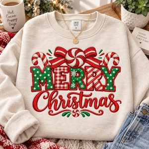 May include: A beige crewneck sweatshirt featuring a festive graphic with the text Merry Christmas. The design includes red and green candy canes, a peppermint swirl, and a red bow. The word Merry is in green and red patterns.