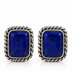 May include: A pair of rectangular cufflinks featuring deep blue lapis lazuli stones with natural gold-colored flecks. Each stone is set within a polished silver-toned metal frame that has a decorative twisted rope border design around the edge.