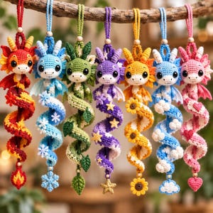 May include: Seven crocheted dragon ornaments hanging in a row, each featuring a unique color scheme and themed charm at the bottom, including a flame, snowflake, leaf, star, sunflower, cloud, and heart, all suspended by matching yarn loops.