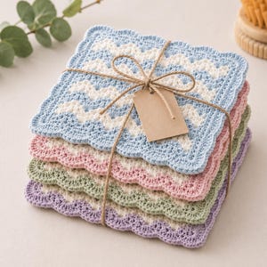 May include: A stack of four square crochet coasters featuring a wavy pattern in white paired with light blue, pink, sage green, and lavender. The coasters are tied together with brown twine and include a blank, rectangular brown paper tag.