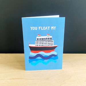 May include: A blue card with the text "You float my" and a cartoon illustration of a red, white and black cruise ship with green flags on the top of the ship. The ship is floating on blue and dark blue waves.