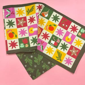 May include: Two green fabric table runners with a Christmas theme. One runner features a repeating pattern of red, yellow, pink, and green squares with various Christmas icons. The other runner features a repeating pattern of green pine branches and white snowflakes.