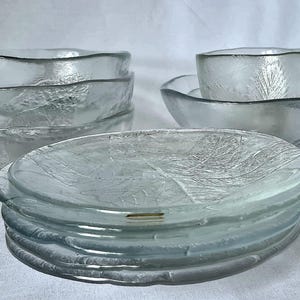 Könnte beinhalten: Ein Set aus klarem Glasgeschirr mit strukturiertem Blattmuster. Das Set besteht aus einem Stapel runder Teller, mehreren ineinander gestapelten tiefen Schüsseln sowie einer kleinen Schale in einer flachen Schale, alles mit matter Optik.