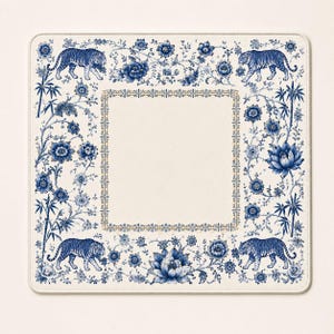 May include: A square placemat featuring a cream-colored center bordered by a decorative frame. The outer edge displays a blue and white pattern of tigers, blooming flowers, and bamboo stalks arranged in a symmetrical, repeating botanical design.