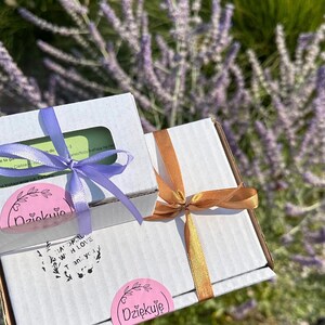 May include: Two white cardboard shipping boxes tied with ribbon. The smaller box has a light purple ribbon and a pink sticker reading Dziękuję. The larger box has a bronze ribbon and a pink sticker reading Dziękuję, plus text reading Handmade with love Thank you.