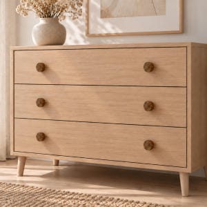 May include: A light-toned wooden dresser featuring three horizontal drawers, each equipped with two circular, dark-colored knobs. The furniture piece stands on four tapered legs and displays a natural wood grain finish throughout its structure.