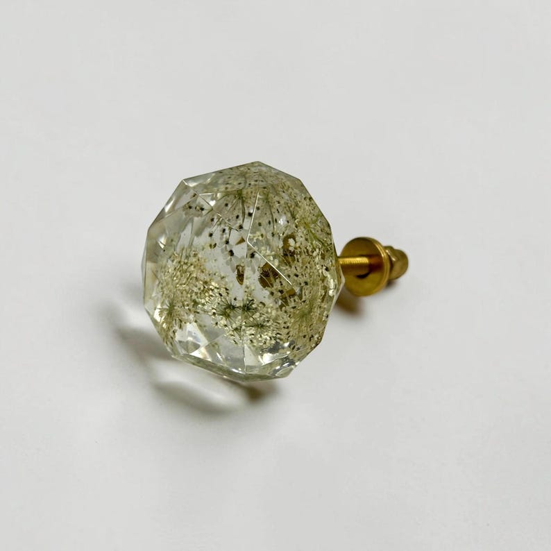May include: A faceted, clear resin cabinet knob with a spherical shape, containing embedded dried white dandelion seeds. The knob features a gold-toned metal base and a threaded screw attachment extending from the back for mounting purposes.