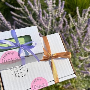 May include: Two white cardboard shipping boxes with lids. The smaller box has a light purple ribbon and a pink sticker reading Dziękuję. The larger box has a copper ribbon and a pink sticker reading Dziękuję, with text reading Handmade with love, Thank you.