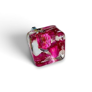 May include: A square cabinet knob made of clear resin with embedded vibrant pink flower petals. The knob features a smooth, glossy finish and a metallic mounting screw visible at the back, providing a functional hardware piece for furniture.