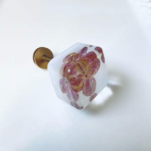 May include: A square cabinet knob made of clear resin with embedded dried pink and purple hydrangea petals. The knob features a brass-colored metal screw and base attachment extending from the back, providing a functional mounting point.