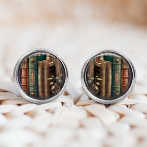 Peut inclure: Une paire de boucles d'oreilles en argent avec un cabochon rond en verre représentant une image de style vintage d'une pile de livres reliés en cuir avec des accents dorés.
