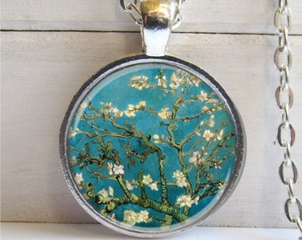 May include: A silver necklace with a round pendant featuring a painting of a blooming almond tree with white flowers against a blue sky. The pendant is framed in silver.