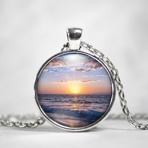 Pode incluir: Um colar de prata com um pingente redondo de vidro que apresenta uma fotografia de um pôr do sol sobre o oceano. O pingente tem um diâmetro de aproximadamente 2,5 cm.