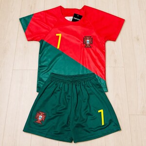 Puede incluir: Un conjunto de fútbol rojo y verde que incluye una camiseta y pantalones cortos, ambos con el número 7 en amarillo. La camiseta muestra el escudo de la selección nacional de Portugal en el pecho, mientras que los pantalones cortos llevan el mismo escudo en la pierna derecha.