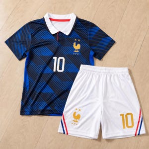 Peut inclure: Un maillot de football bleu foncé avec un col blanc, des rayures noires diagonales et le numéro 10 en blanc. Il présente un emblème de coq doré avec deux étoiles au-dessus. Accompagné d'un short de football blanc avec le numéro 10 et un coq doré.