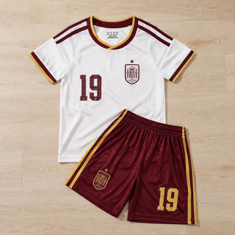 May include: A white short-sleeved jersey with a maroon and gold collar, featuring the number 19 in maroon and a crest on the chest. Paired with maroon athletic shorts featuring gold side stripes, the number 19 in gold, and a matching crest emblem.