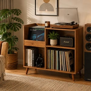 May include: A wooden record player console with four open storage compartments. The top surface holds a turntable, a candle, and a potted plant. The shelves contain vinyl records, books, and a small black figurine. A speaker stands to the right.
