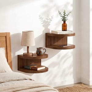 May include: Two semi-circular floating wooden shelves mounted on a wall. The lower shelf holds a lamp with a beige shade and a ceramic mug. The upper shelf holds a glass bottle with greenery and books. A smartphone rests on the upper shelf.