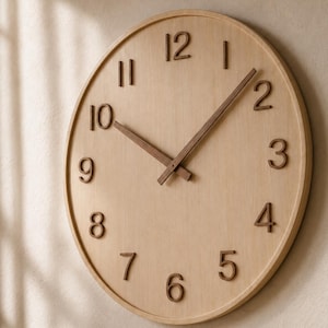 May include: A round wall clock with a light wood grain face and a matching circular frame. The clock features raised, dark brown numerals from 1 to 12 and two matching dark brown hands indicating the time, mounted on a flat, circular surface.
