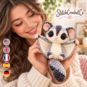May include: A handmade crochet sugar glider plush toy featuring a grey and cream color scheme, large black safety eyes, pink inner ears, and a long textured tail. The toy has a soft yarn texture and is held in place, displaying its wings.