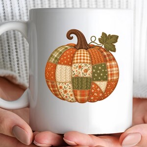 Peut inclure: Un mug en céramique blanche orné d'un motif central représentant une citrouille composée de divers motifs en patchwork dans des tons orange, vert et crème, incluant des imprimés floraux, des textures en tricot torsadé et des carreaux.