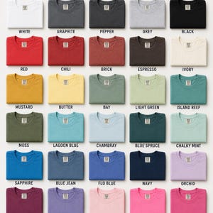 Op de afbeelding: Een Comfort Colors kleurenkaart met twee&euml;ndertig gevouwen t-shirts in diverse tinten, waaronder wit, grafiet, pepper, grijs, zwart, rood, chili, brick, espresso, ivoor, mosterd, boter, bay, lichtgroen, island reef, mos, lagoon blue, chambray, blue spruce, chalky mint, saffier, blue jean, flo blue, marineblauw, orchidee, bes, violet, blossom, neonroze, crunchberry, watermeloen, yam en karmozijnrood.