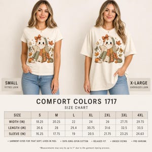 Op de afbeelding: Een cr&egrave;mekleurig t-shirt met een afbeelding van een geest met een strik, omringd door herfstbladeren en pompoenen. Het t-shirt wordt getoond in een kleine getailleerde look en een extra grote oversized look, inclusief een Comfort Colors 1717 maattabel.