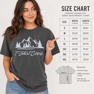 Op de afbeelding: Een antracietgrijs t-shirt met korte mouwen en een lichtblauwe afbeelding van bergen, dennenbomen en vogels boven de tekst T-Shirt Cove. Een maattabel toont de breedte- en lengtematen in inches voor de maten S tot en met 4XL.