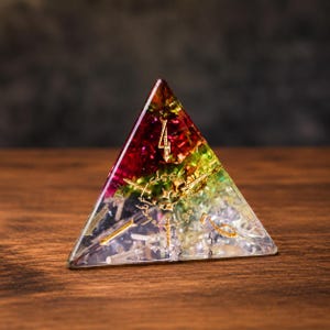 May include: A four-sided pyramid-shaped die featuring a translucent resin body with a gradient of red, green, and clear sections. The die contains embedded gold-colored metallic flakes and features gold-colored engraved numbers on its faces.