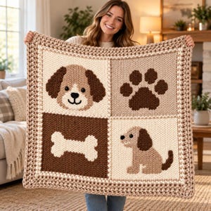 May include: A square, chunky knit blanket featuring a four-panel design in shades of cream and brown. The panels display a puppy face, a paw print, a dog bone, and a sitting puppy. The blanket is finished with a textured, multi-coloured border.