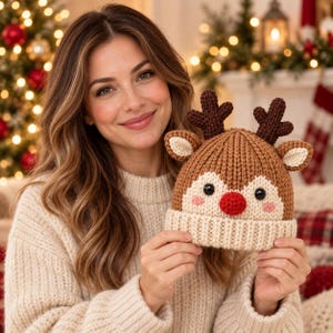 May include: A brown and cream knit beanie featuring a reindeer design with dark brown antlers, cream-colored ears, black button eyes, and a bright red nose. The hat has a thick ribbed cuff and a textured knit pattern throughout the main body.