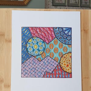 Peut inclure: Un dessin carr&eacute; sur papier blanc pr&eacute;sentant un motif g&eacute;om&eacute;trique vibrant compos&eacute; de plusieurs sections. Le design inclut des motifs complexes dessin&eacute;s &agrave; la main dans des tons de bleu, rouge, orange et jaune, avec des cercles et des lignes.
