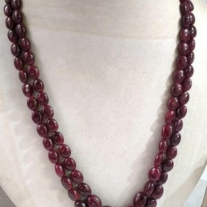 Puede incluir: Un collar de doble hebra con cuentas lisas de forma ovalada en color burdeos intenso. Las cuentas son uniformes en tamaño y forma, ensartadas para crear dos filas paralelas que caen en un estilo clásico y superpuesto alrededor del cuello.