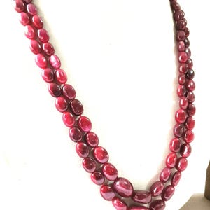 Op de afbeelding: Een dubbelstrengs ketting met gepolijste, ovaalvormige kralen in een diepe, levendige kleur rood. De kralen zijn in twee parallelle rijen geregen, wat een gelaagd effect creëert met een gladde, glanzende afwerking over het gehele sieraad.