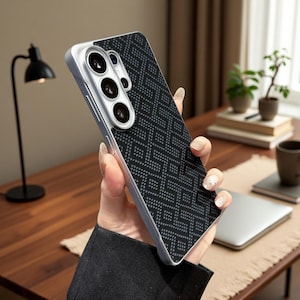 May include: A smartphone case featuring a black back panel with a repeating geometric pattern of small dots. The case has a silver-toned frame and a raised camera module cutout that accommodates three circular lenses and a flash component.