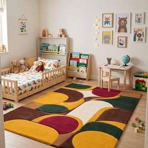 May include: A rectangular area rug featuring a geometric pattern of overlapping circles and semi-circles in shades of mustard yellow, deep forest green, dark brown, and cream. The rug has a thick, plush texture and covers a light-colored wooden floor.