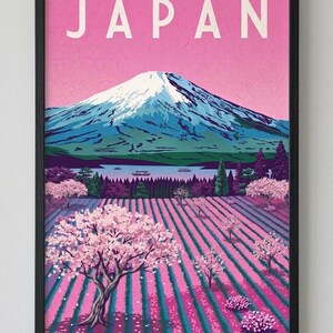 Puede incluir: Una lámina artística enmarcada que muestra un paisaje estilizado del monte Fuji bajo un cielo rosa con la palabra JAPAN en letras blancas. La escena incluye un lago, árboles de color verde oscuro y filas de cerezos en flor en un campo con rayas rosas y verde azulado.
