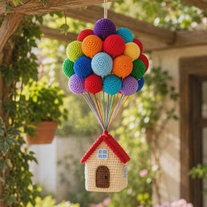 May include: A crochet hanging decoration featuring a small beige house with a red roof suspended by numerous colorful yarn strings attached to a cluster of round, multi-colored crochet spheres representing a large bunch of balloons.