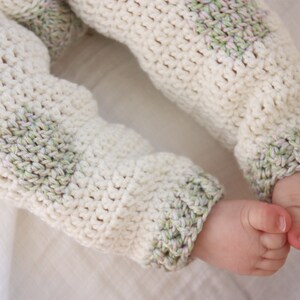 May include: White crocheted baby pants with green and white stripes on the cuffs.