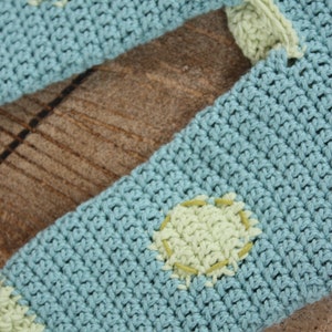 May include: A light blue crocheted sweater with green polka dots. The sweater is made with a soft, textured yarn.
