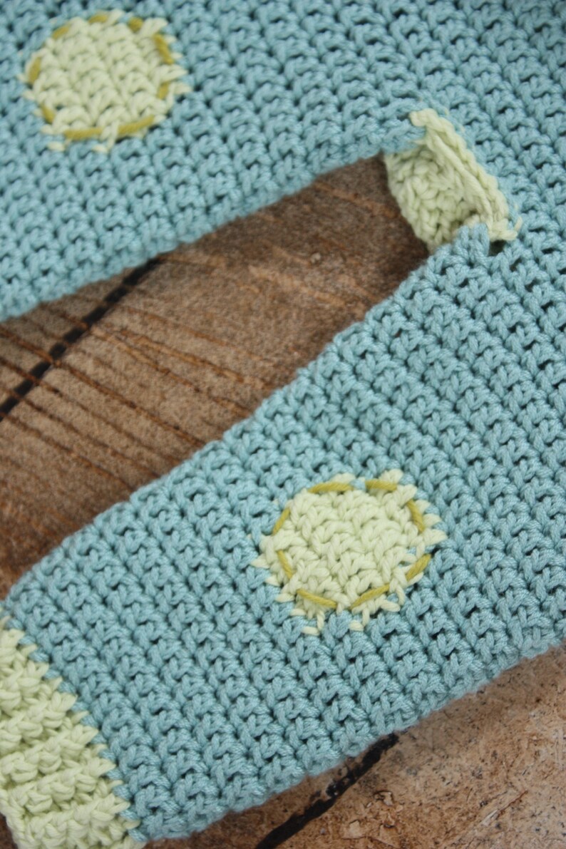 May include: A light blue crocheted sweater with green polka dots. The sweater is made with a soft, textured yarn.