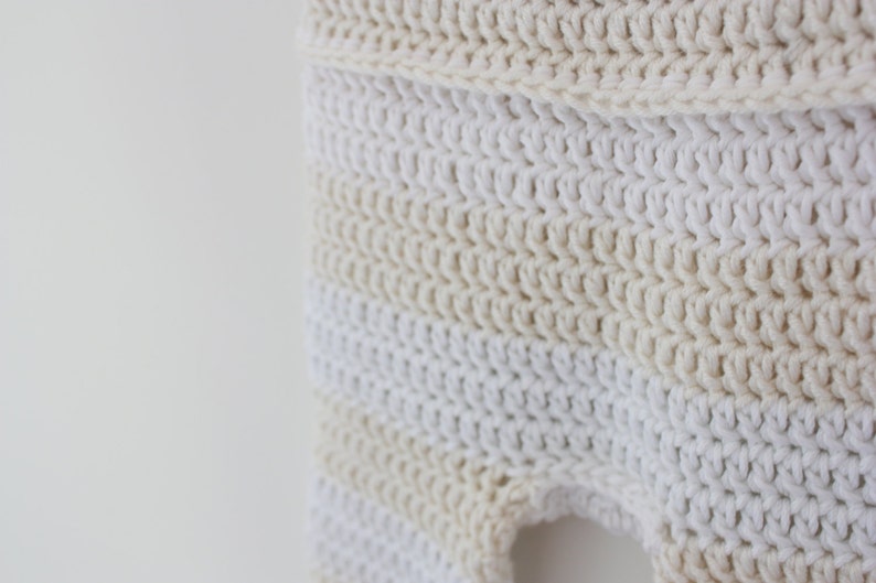 May include: Close-up of a crocheted garment in cream and white. The handmade item features a textured stitch pattern with horizontal stripes of varying shades of cream and white. The garment appears to be a baby item.