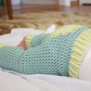 May include: A baby wearing a crocheted outfit with a blue and yellow color scheme. The outfit is made of soft yarn and has a loose fit.