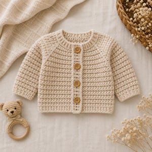 Könnte beinhalten: Eine beigefarbene Langarmstrickjacke aus strukturiertem Häkelstoff. Das Kleidungsstück verfügt über einen Rundhalsausschnitt und eine Knopfleiste auf der Vorderseite mit vier runden Holzknöpfen. Die Ärmel sind lang und das Design ist schlicht.