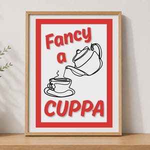 May include: A rectangular wall art print in a light wood frame featuring a red border and the red text Fancy a CUPPA. The centre displays a black continuous line drawing of a teapot pouring liquid into a teacup on a saucer with steam rising.