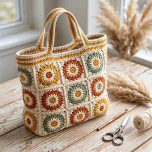 May include: A crochet tote bag constructed from square panels featuring circular floral motifs in shades of mustard yellow, burnt orange, and sage green on a cream background, with two matching handles and a reinforced top border.