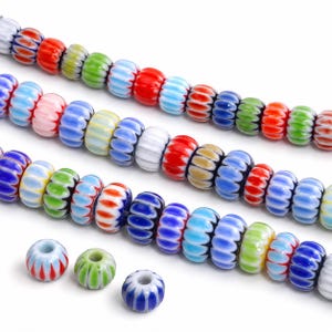 May include: Three strands of multi-coloured glass beads arranged horizontally, featuring a repeating vertical ribbed pattern in shades of red, blue, green, white, and yellow, with three individual loose beads placed below the strands.