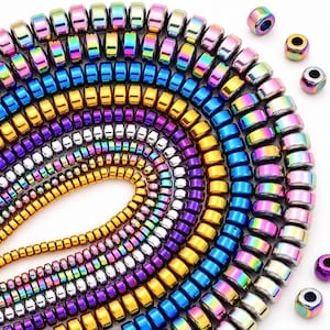 May include: A collection of round, disc-shaped beads arranged in concentric, curved rows. The beads feature a metallic, iridescent finish in vibrant shades of rainbow, gold, blue, purple, and silver. Several individual beads are scattered nearby.