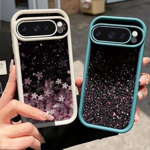 May include: Two rectangular phone cases with raised camera bumpers. The left case is cream-colored with a black background featuring pink cherry blossoms and white sparkles. The right case is teal with a black background and pink glitter.